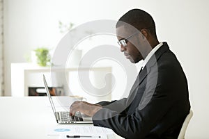 Focused black worker working at laptop at company workplace