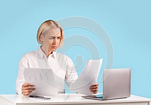 Focused business lady working with documents near laptop computer at her desk against blue background, copy space