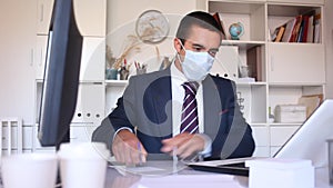 Focused businessman in disposable face mask working on laptop in office. Necessary precautions during COVID 19 pandemic