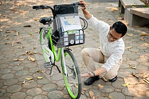 A focused businessman inspects his bicycle tire in a park, encountering an issue during his commute