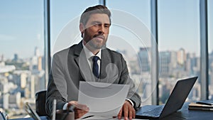Focused businessman looking papers at desk. Smiling inspired man typing laptop