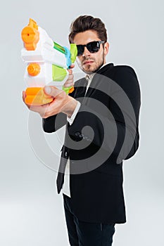 Focused businessman in sunglasses and suit shooting with water gun