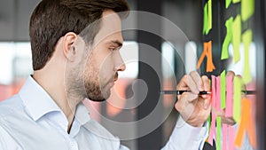 Focused businessman writing on sticky notes attached on glass wall