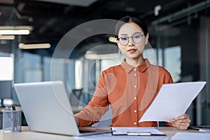Focused businesswoman analyzing documents at her modern office desk