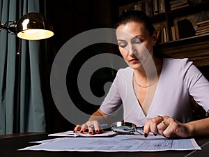 Focused businesswoman sitting at office desk and checking a engineering drawing with a magnifier. Business Auditor Using