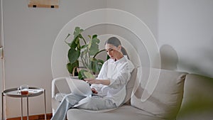 Focused businesswoman typing laptop home couch. Relaxed girl chatting computer