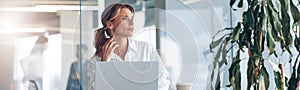 Focused businesswoman working on laptop and looking out the window at workplace at modern office