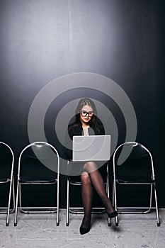 Focused businesswoman working on laptop while waiting for interview sitting on chair