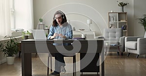 Focused busy student woman in wireless headphones writing learning notes