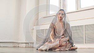 Focused and calm ballerina putting on pointe shoes sitting on grey stone floor