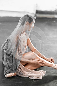 Focused and calm ballerina putting on pointe shoes sitting on grey stone floor