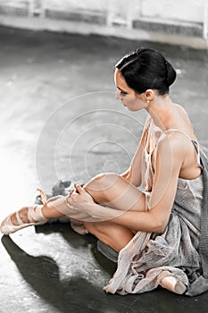 Focused and calm ballerina putting on pointe shoes sitting on grey stone floor