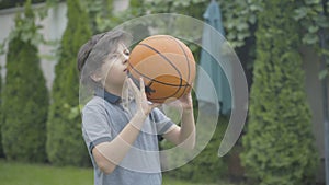 Focused Caucasian brunette boy throwing ball and making victory gesture. Portrait of happy cute kid rejoicing outdoors