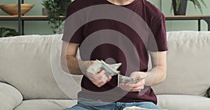 Focused Caucasian Man Counting Cash on Sofa in the Living Room