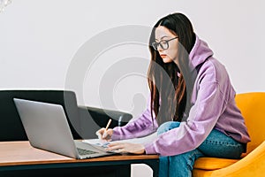 Focused caucasian young woman college student in eyeglasses studying with laptop distantly preparing for test exam writing essay photo