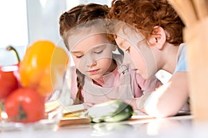 focused children reading cookbook while cooking together