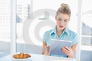 Focused classy woman using tablet while having breakfast