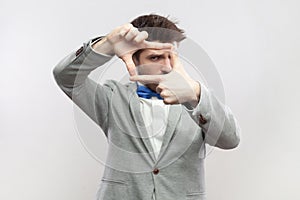 Focused concentrated bearded man standing looking at camera through frame from fingers, making photo