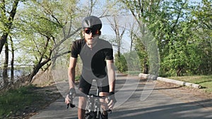 Focused confident cyclist pedaling out of the saddle. Front follow shot. Professional cyclist wearing black outfit on bicycle.