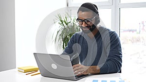 Focused confident male Indian remote consultant wearing headset using laptop