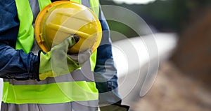 A focused construction worker holds a yellow helmet and green vest, Safety gear, construction site, industrial work image