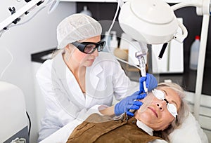 Focused cosmetologist performing laser resurfacing to senior woman