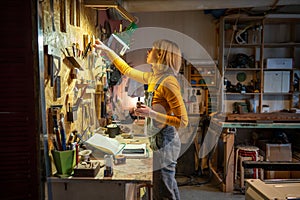 Focused craftswoman carpenter arranging tools on workshop wall after making wooden DIY furniture.