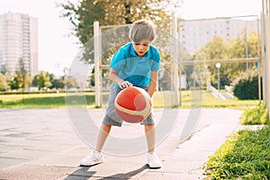 Focused cute boy athlete leads the ball in a game of basketball. A boy plays basketball after school.