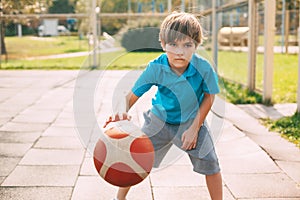 Focused cute boy athlete leads the ball in a game of basketball. A boy plays basketball after school. Sports, healthy