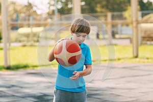 Focused cute boy athlete leads the ball in a game of basketball. A boy plays basketball after school. Sports, healthy