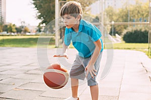 Focused cute boy athlete leads the ball in a game of basketball. A boy plays basketball after school. Sports, healthy