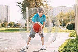 Focused cute boy athlete leads the ball in a game of basketball. A boy plays basketball after school. Sports, healthy