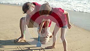 Focused dad and son drawing house in sand with childrens shovel