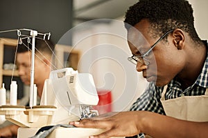 Focused designer sewing fabric. Focused tailor using sewing machine. African American designer sewing a piece of denim