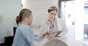 Focused diverse female doctors using tablet and discussing over hospital reception desk, slow motion