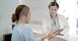 Focused diverse female doctors using tablet and discussing over hospital reception desk, slow motion