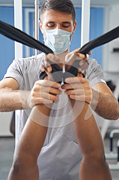 Focused doctor rehabilitating his patient arms using gym equipment
