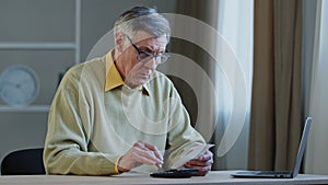 Focused elderly 60s caucasian man sitting at desk manage finances planning budget check bills use internet bank app