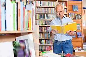 Focused elderly man looking for information in books in bookstore