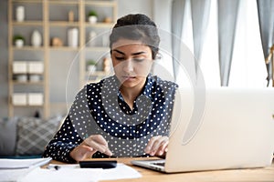 Focused ethnic woman paying bills online on laptop