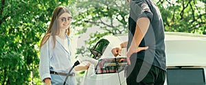 Focused EV car recharging electricity for battery on blurred couple. Exalt