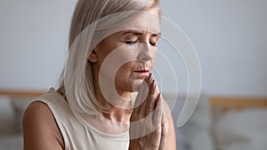 Focused faithful mature woman praying with closed eyes.