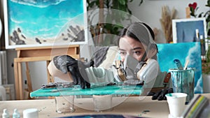 Focused female artist in respirator applying epoxy resin with gloved fingers in art studio closeup