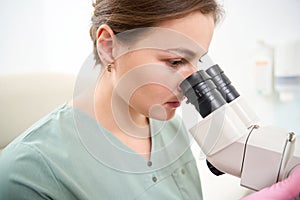 Focused female caucasian doctor wearing medical uniform looking in microscope