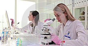 Focused female chemist examines sample through microscope