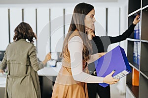 Focused female professionals organizing files in modern office environment, teamwork and efficiency