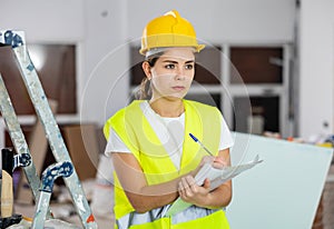 Focused female safety inspector making notes at construction site
