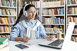 Focused female student studying with headphones in library