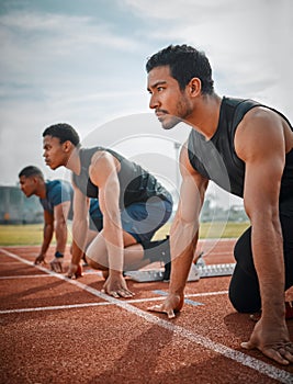 Focused on the finish line. three handsome young male athletes starting their race on a track.