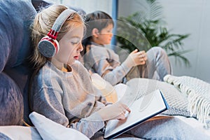 Focused girl in headphones and little boy using digital tablets